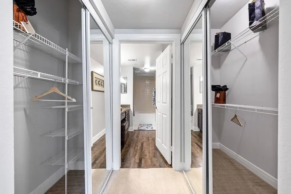 Hallway closet with mirrored doors leads to a bathroom with a bathtub and vanity.