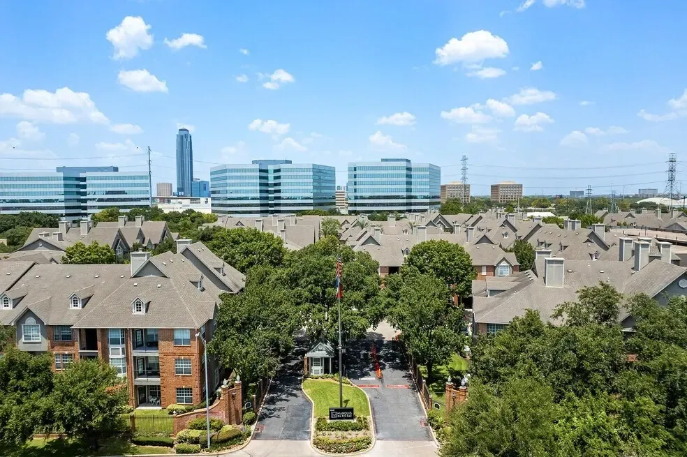 Aerial view of apartment complex entrance with surrounding buildings and trees.
