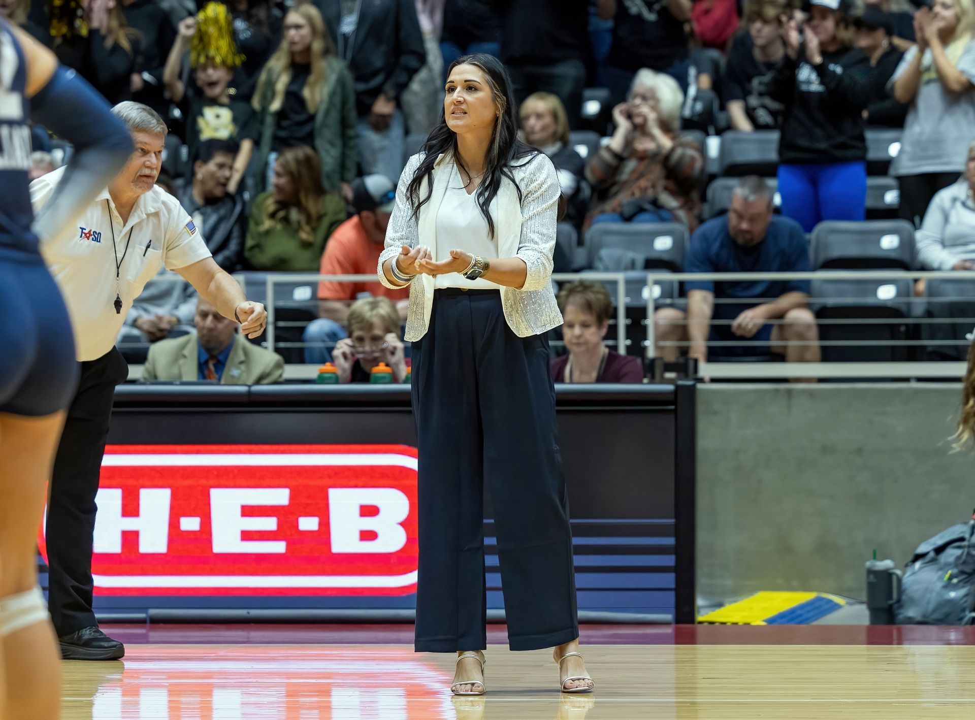 A woman is standing on a basketball court talking to a volleyball player.