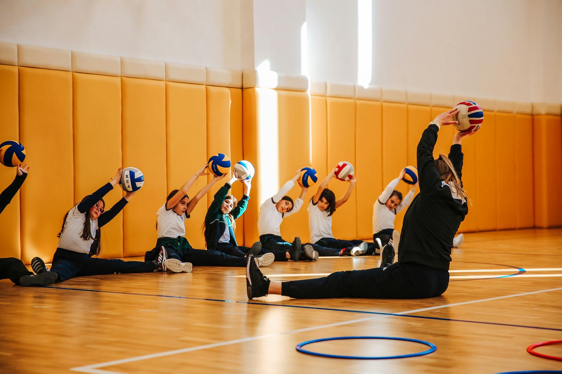 A group of children are doing stretching exercises in a gym.