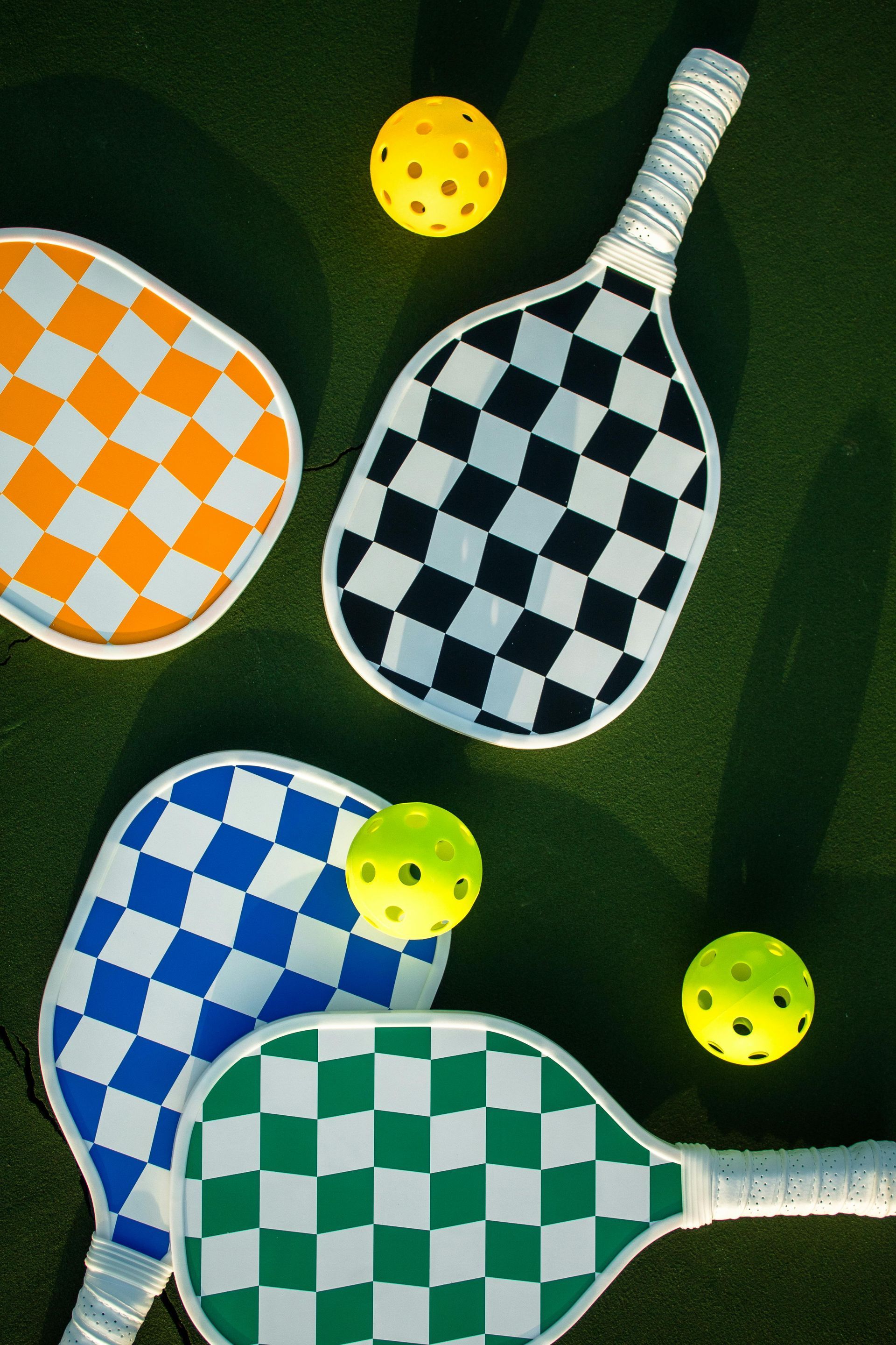 Three paddle tennis rackets with checkered patterns and balls on the grass