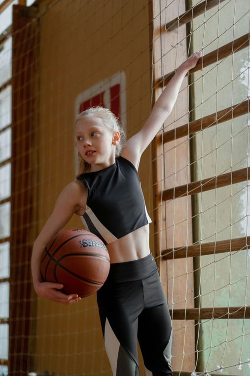 A young girl is holding a basketball in a gym.