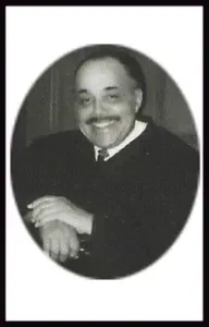 Man in dark suit, smiling, in an oval frame.
