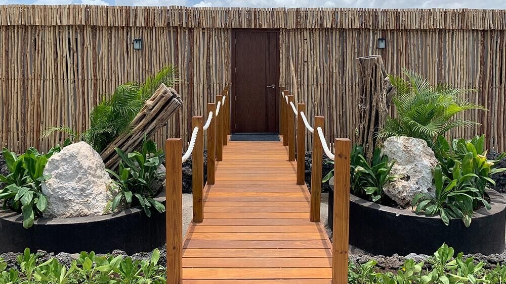 Una pasarela de madera que conduce a un edificio con una valla de bambú.