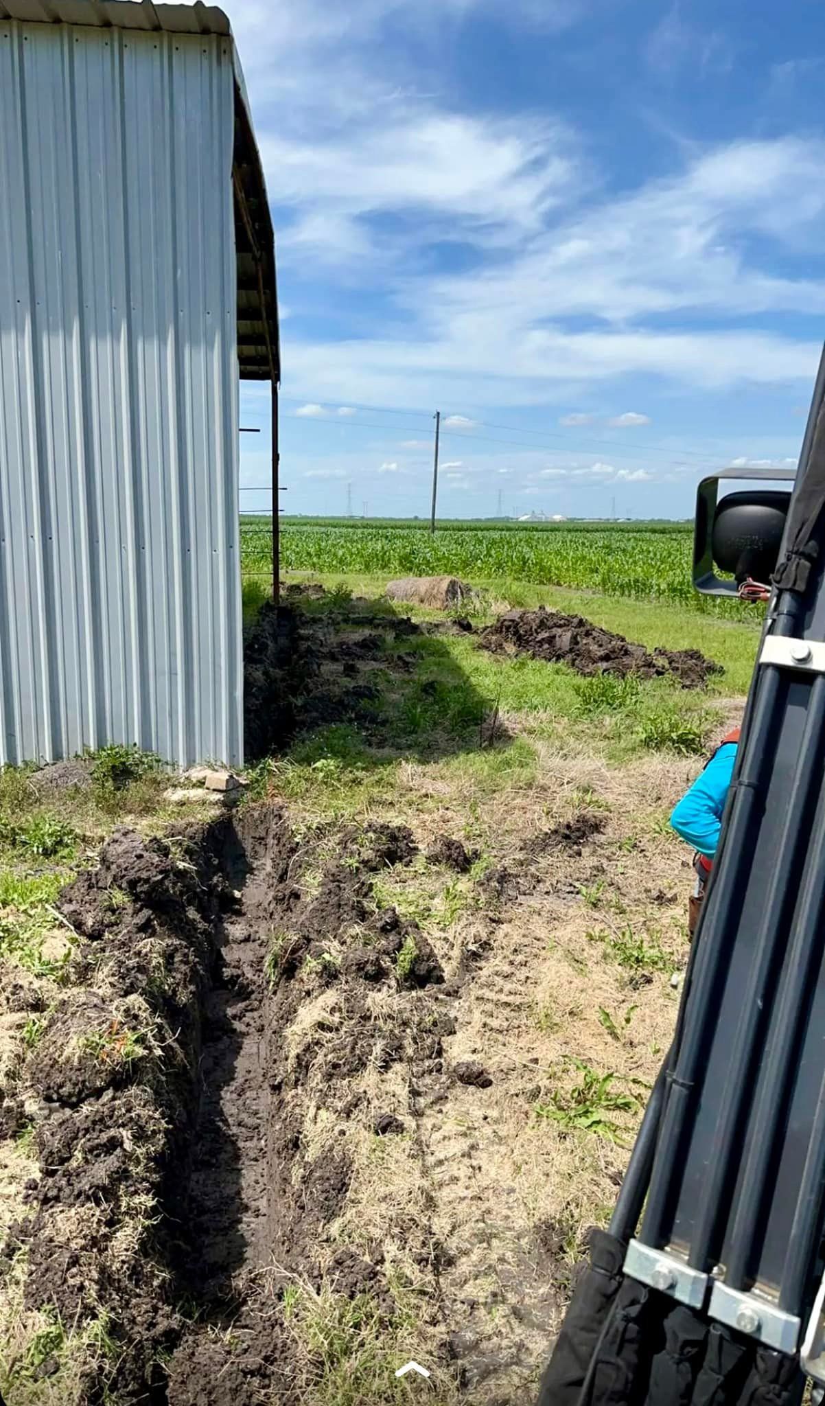A trench dug in the dirt beside a building. Open field and blue sky in the background.