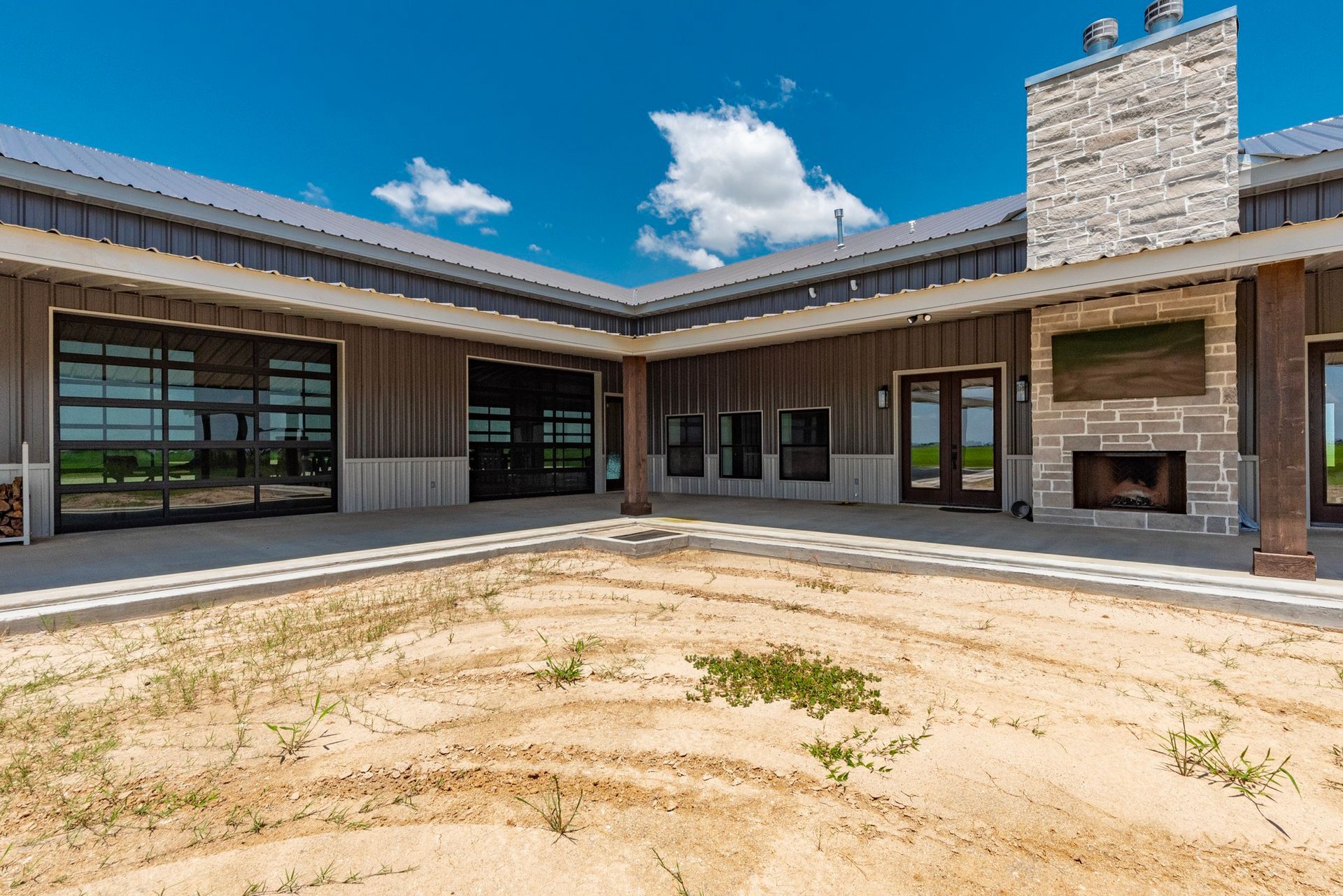 L-shaped modern home with an outdoor patio, fireplace, and glass garage door under a blue sky.