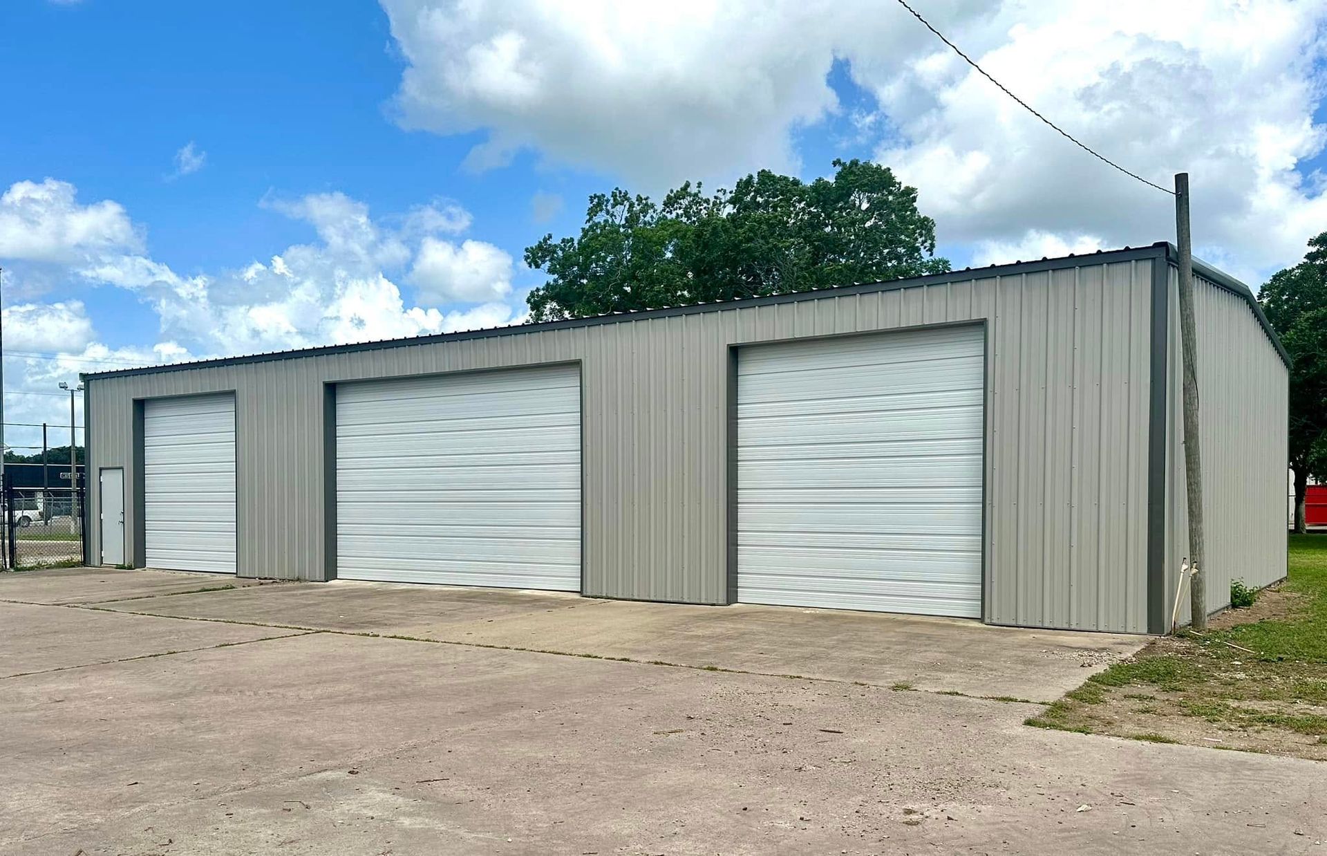 A metal storage building with three garage doors under a blue sky with clouds.