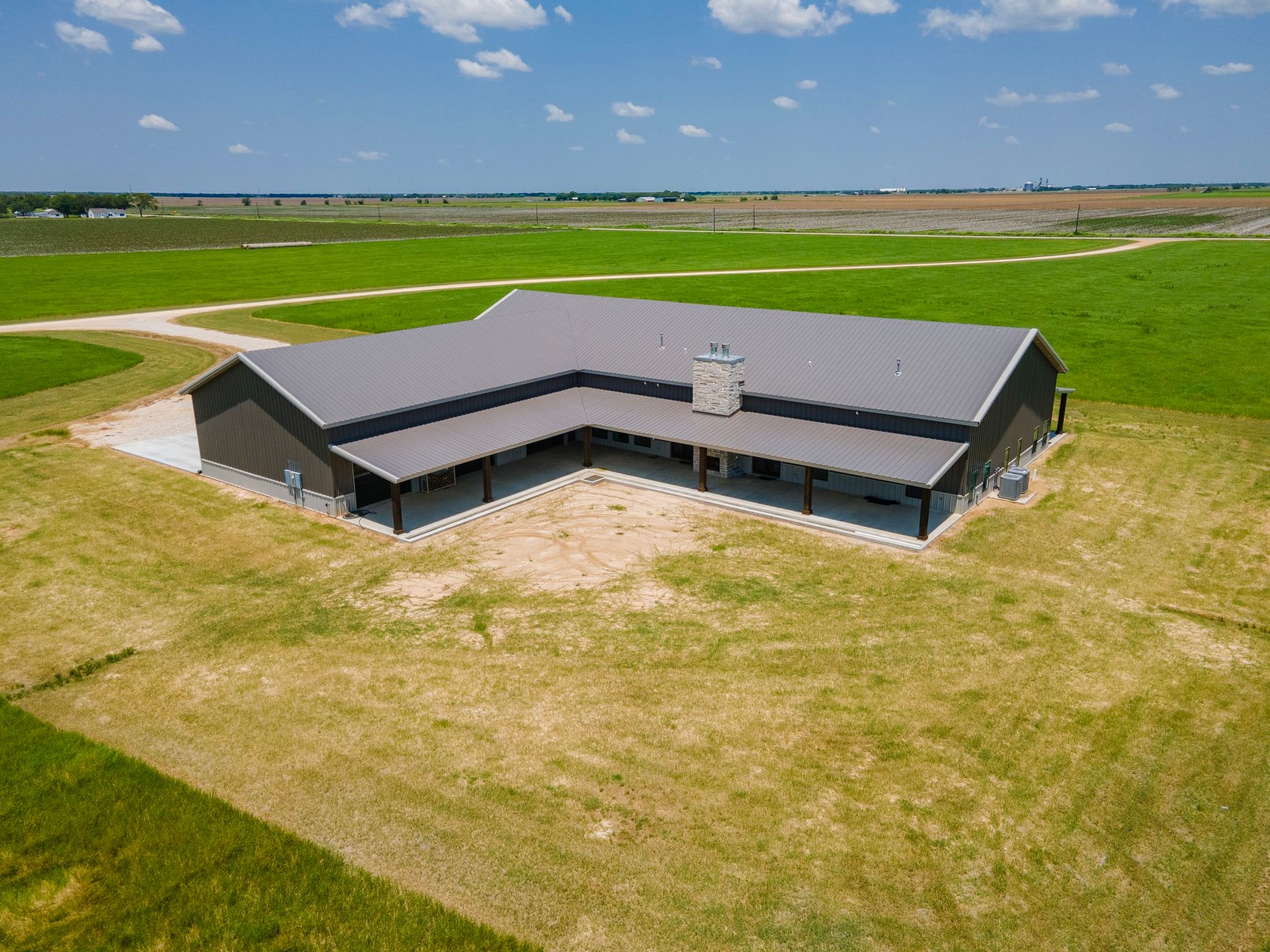 Aerial view of a dark gray metal building in a grassy field on a sunny day.