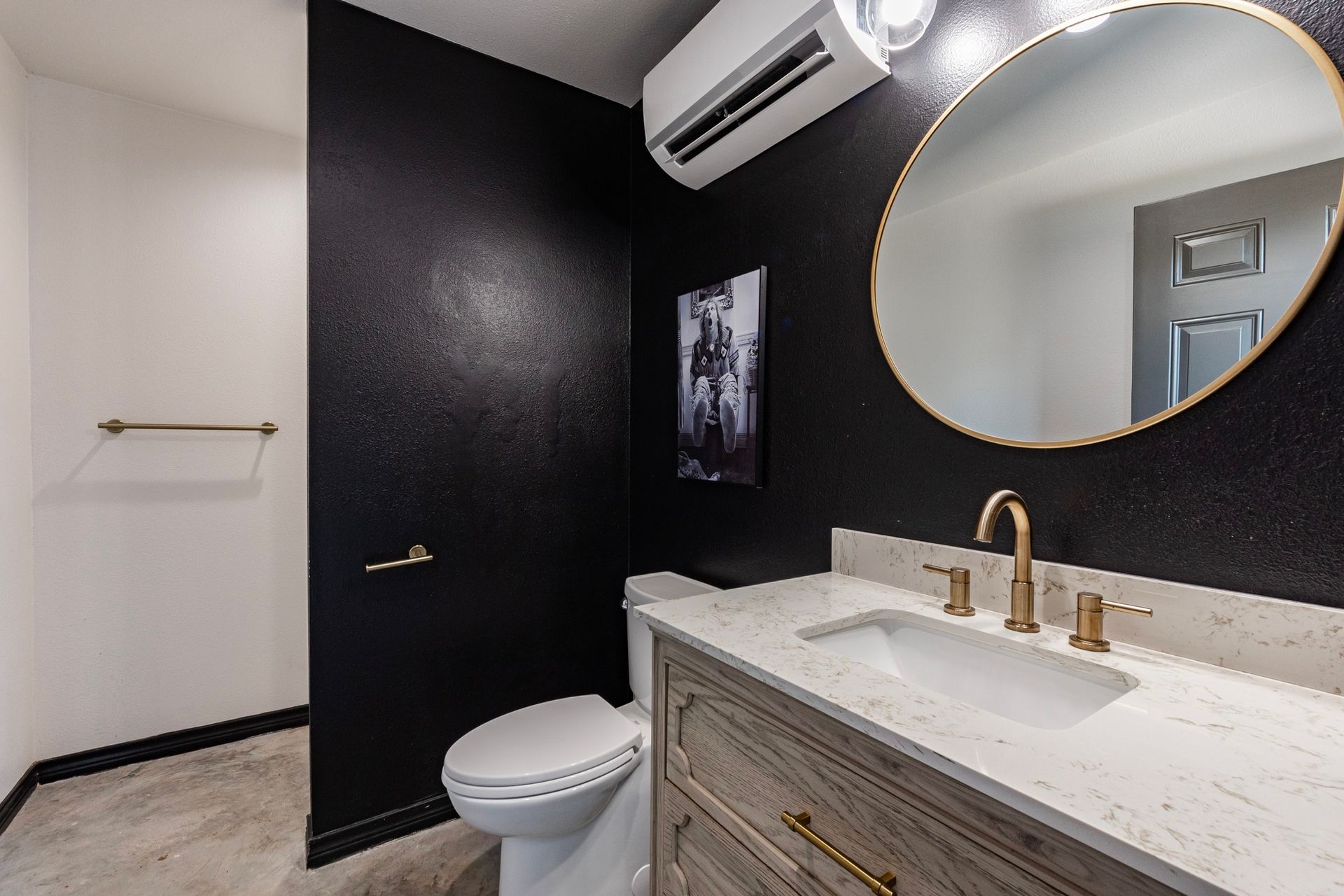 Black-walled bathroom with white countertop, round mirror, gold fixtures, and a toilet.