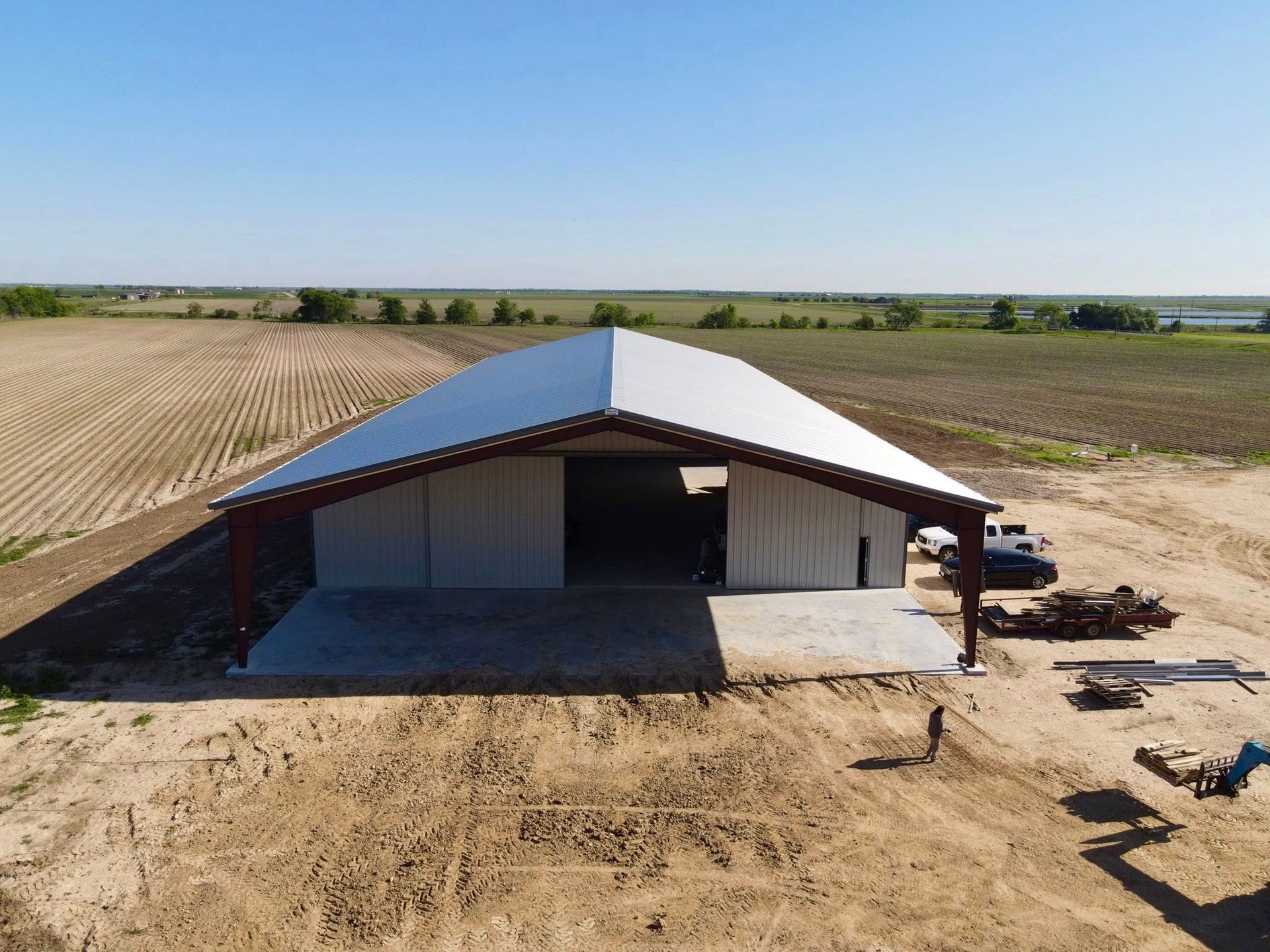 Large metal barn with open front and concrete pad in a rural field.