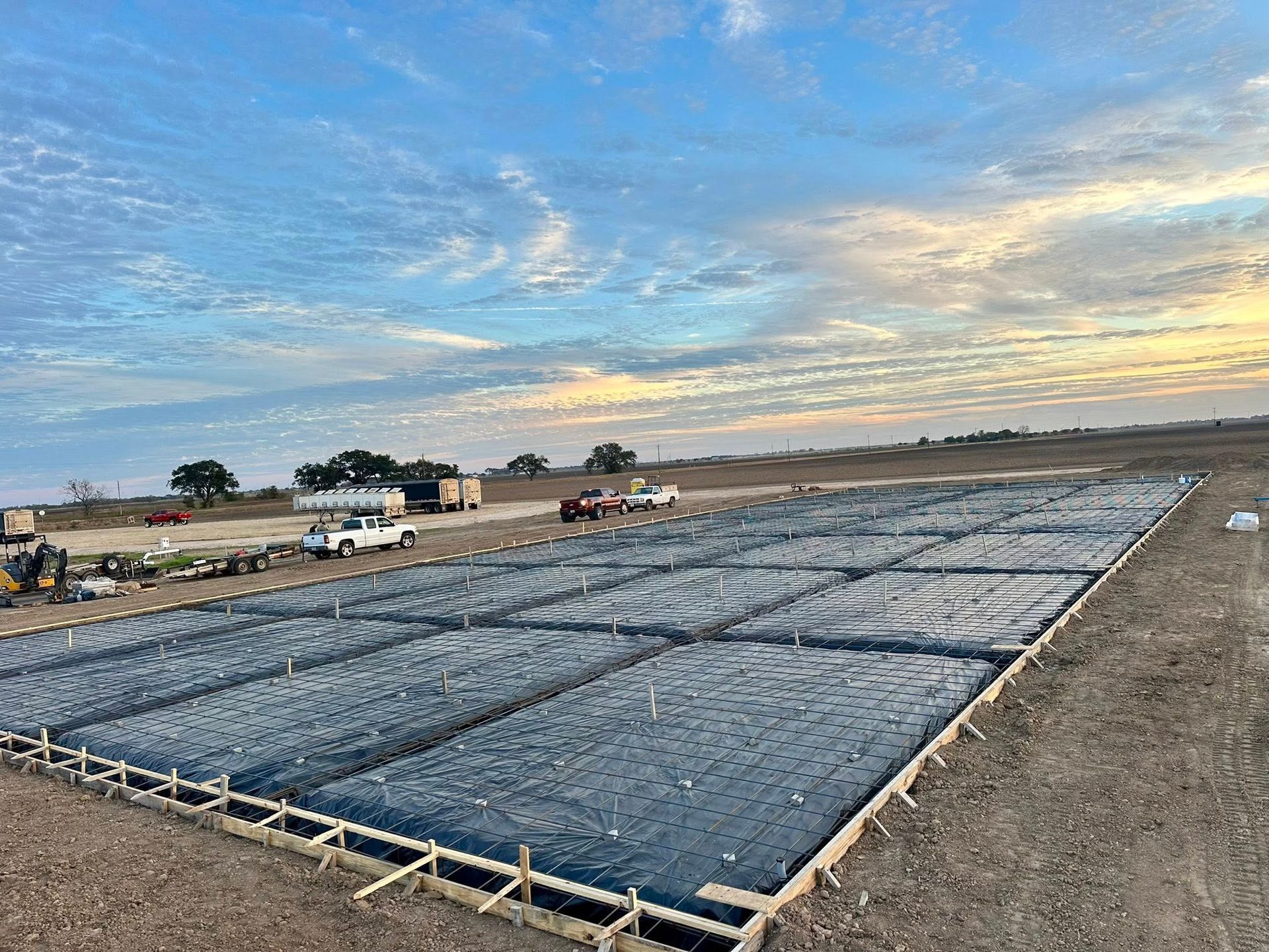 Construction site with a large concrete form, covered with black plastic, under a cloudy sky.