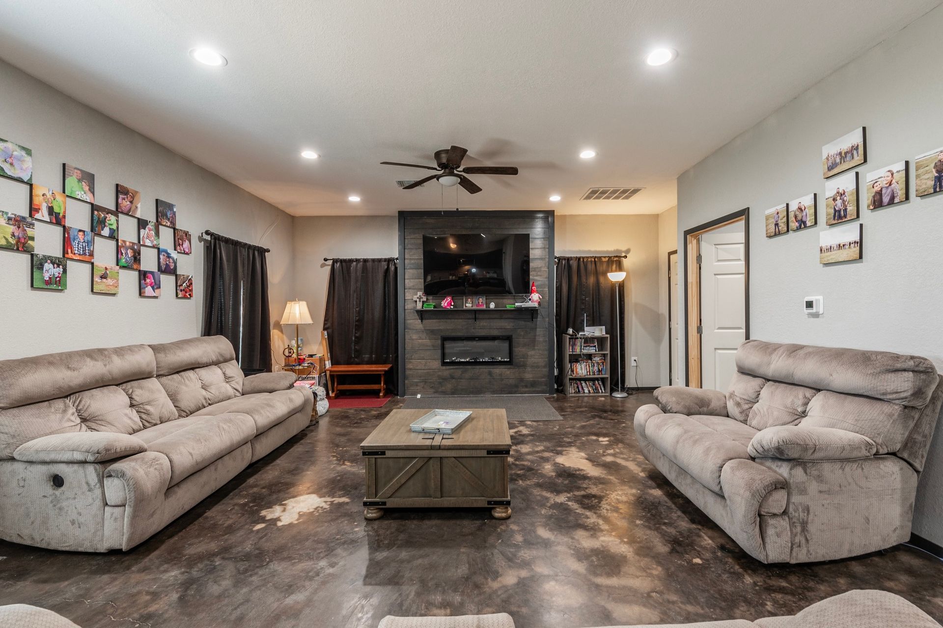 A spacious living room with gray sofas, a fireplace, and photos on the wall.
