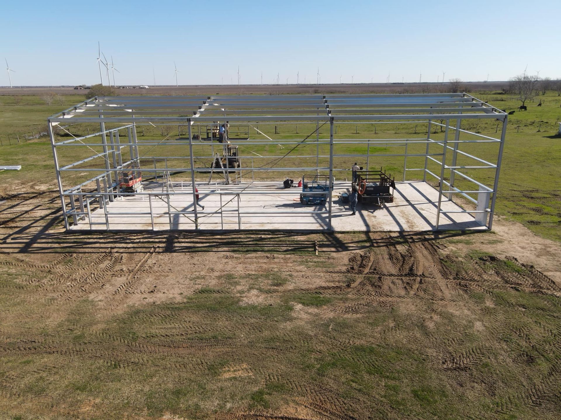 Steel frame of a building under construction on a concrete slab in a field.