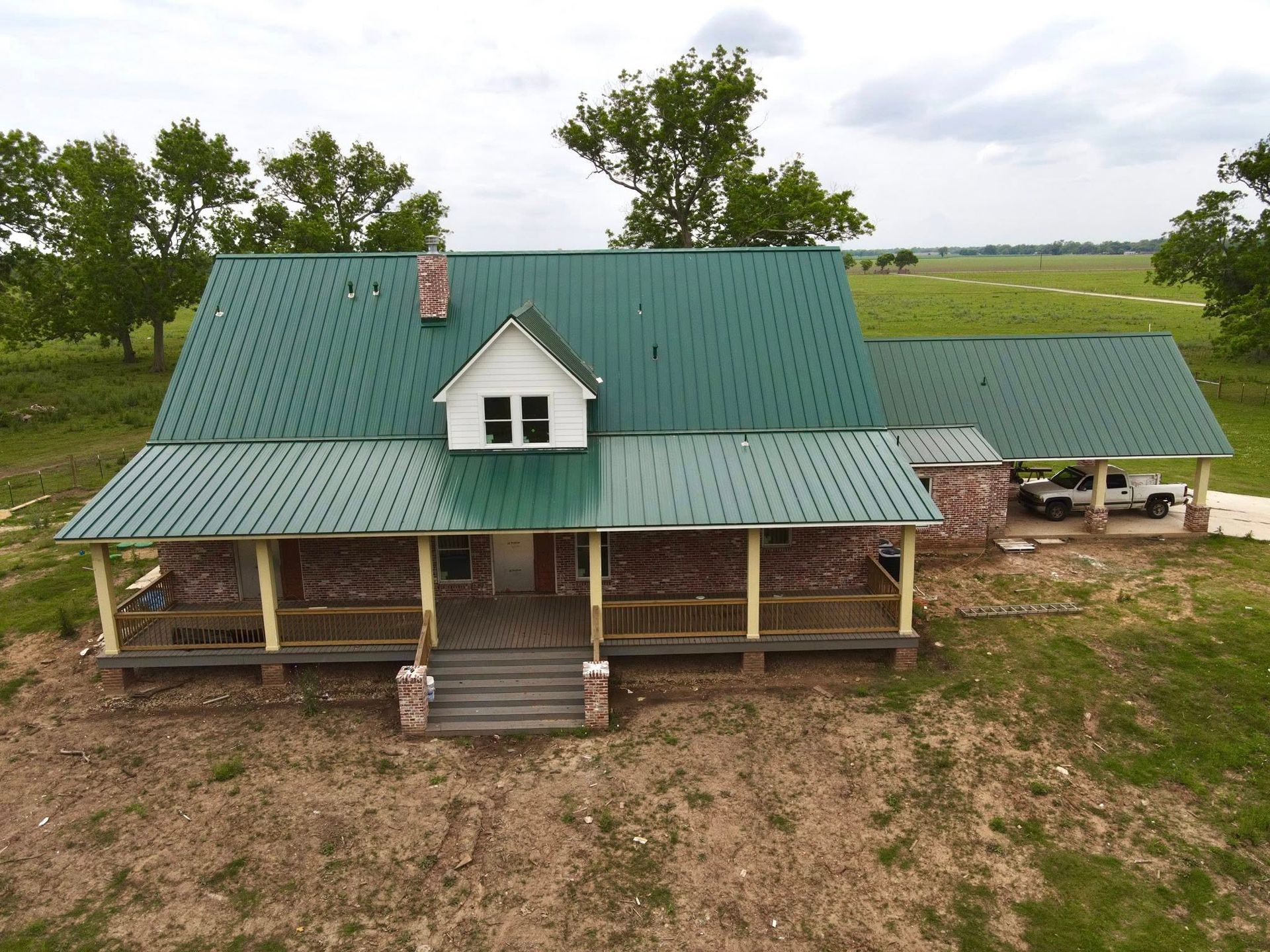 Green-roofed farmhouse with porch, a detached carport, set in a field. Cloudy sky.