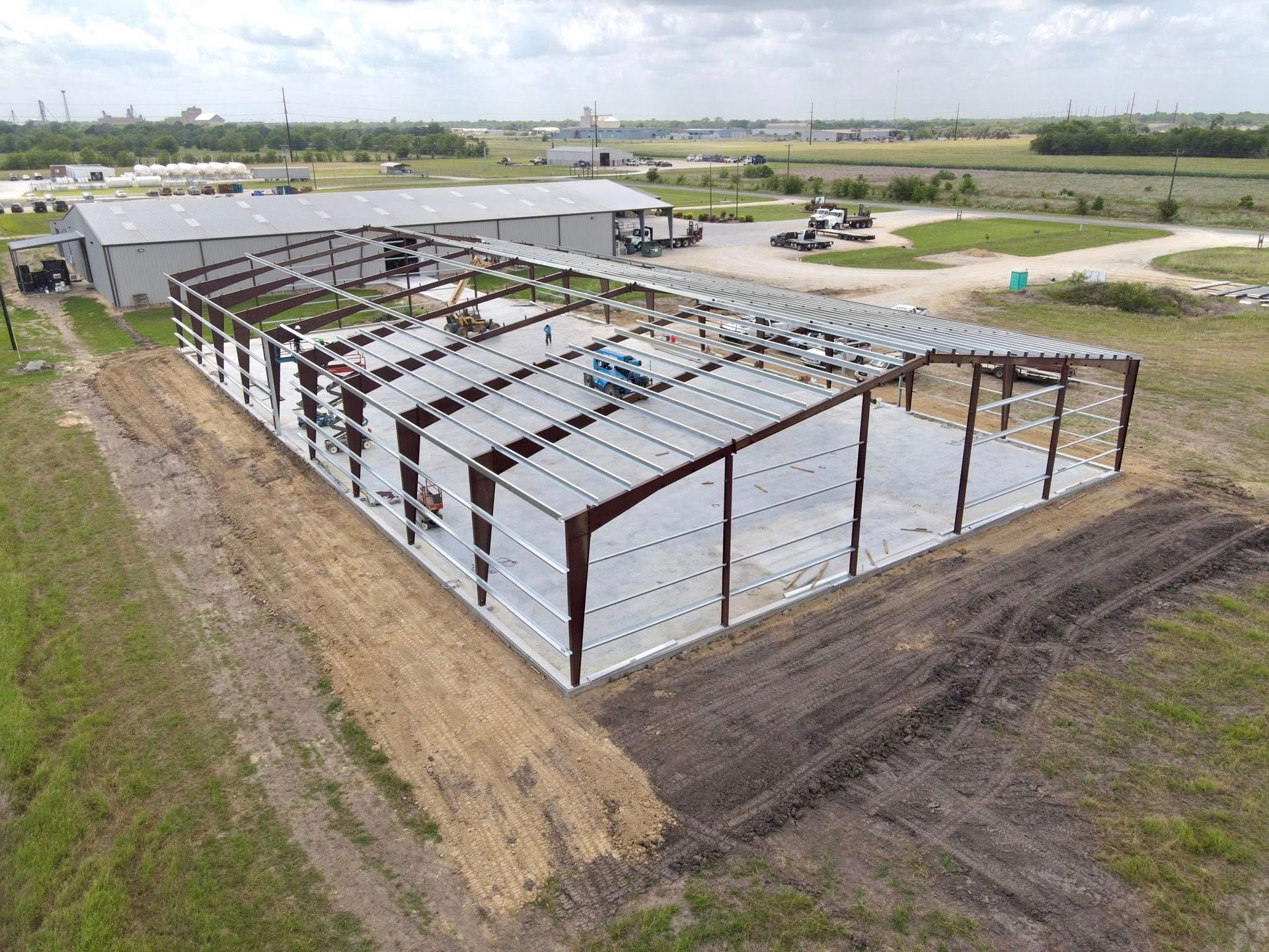 Steel frame of a warehouse under construction on a grassy field. Brown and white building materials.