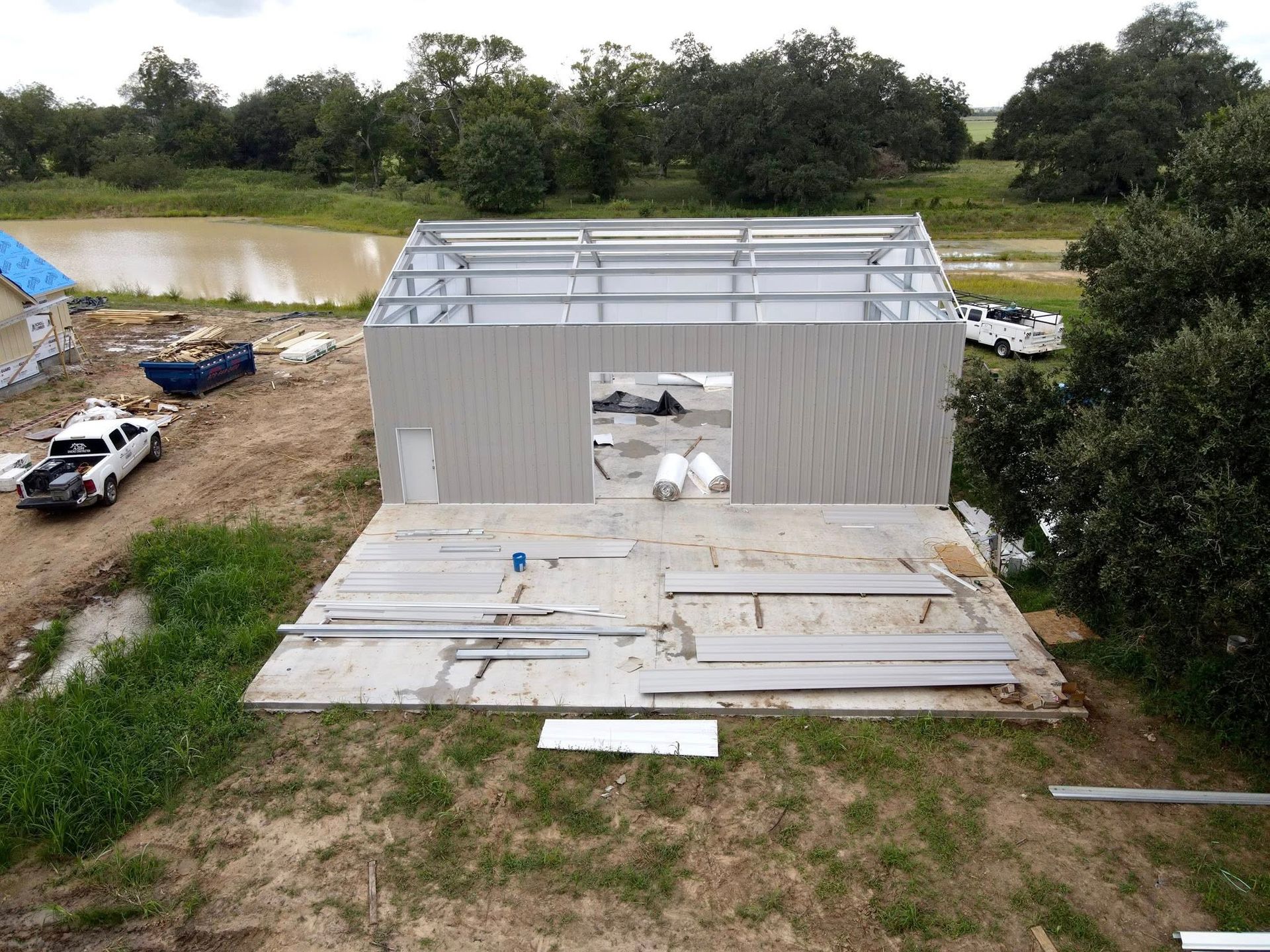 Construction site: partially built metal building with gray siding and frame, concrete slab foundation outdoors.