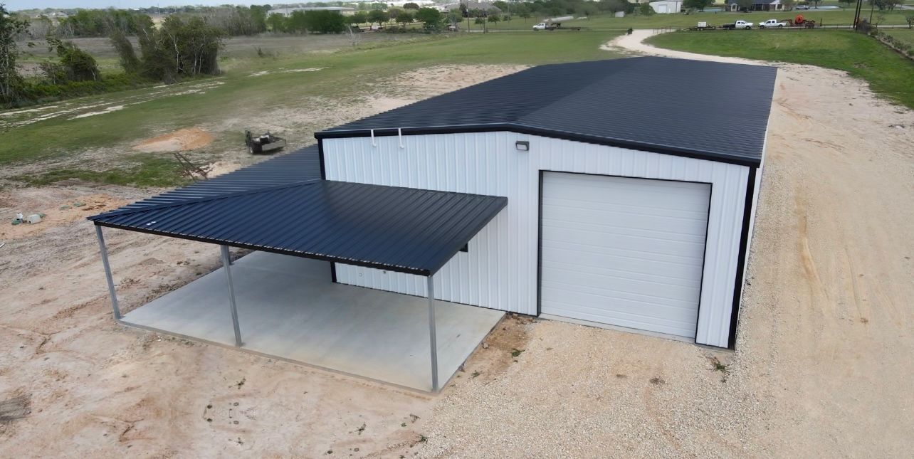 A white metal building with a black roof and carport on a gravel lot.