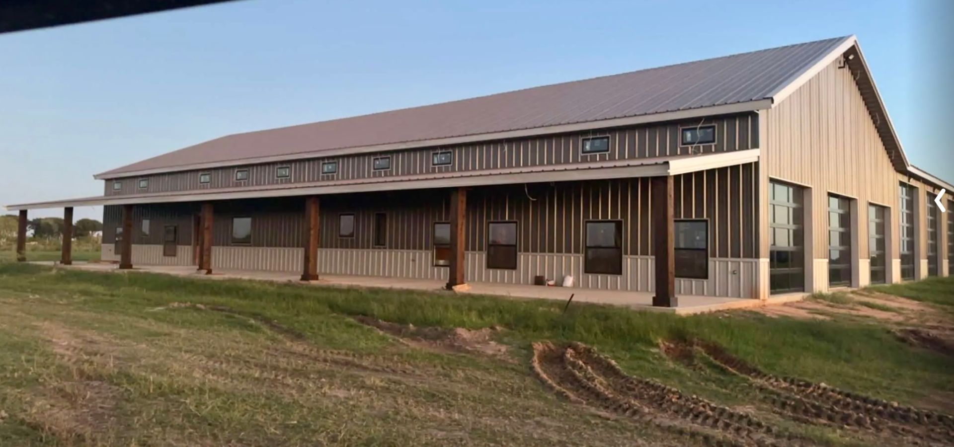 Barn-like building with a porch and windows, set in a grassy field.
