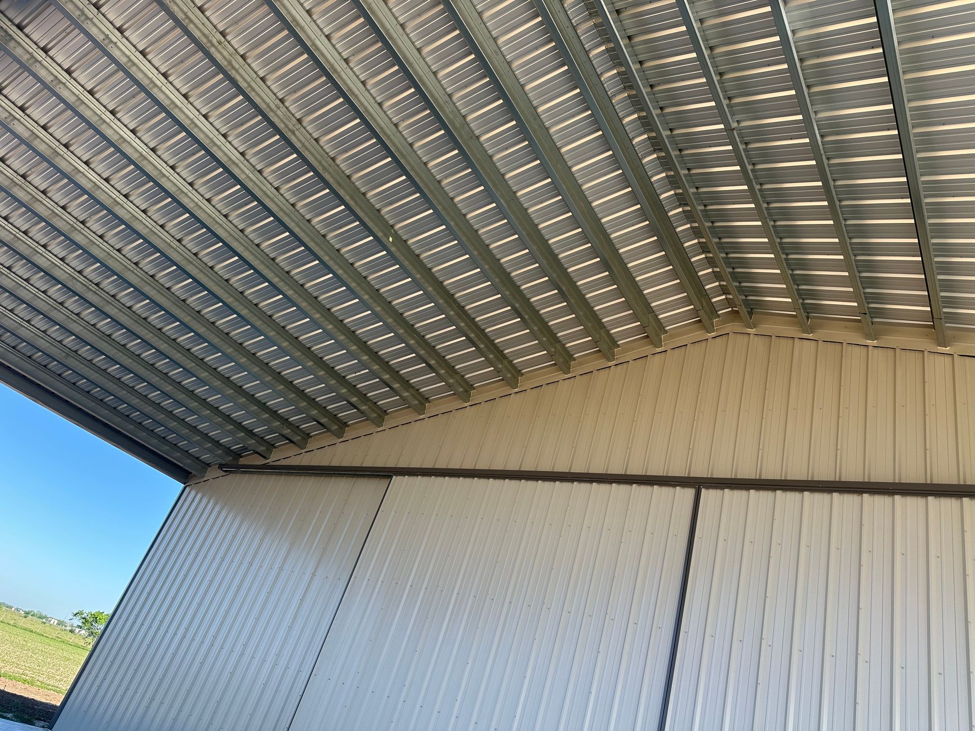 Inside view of a metal shed, showing the corrugated roof and siding. Sunlight shines through.