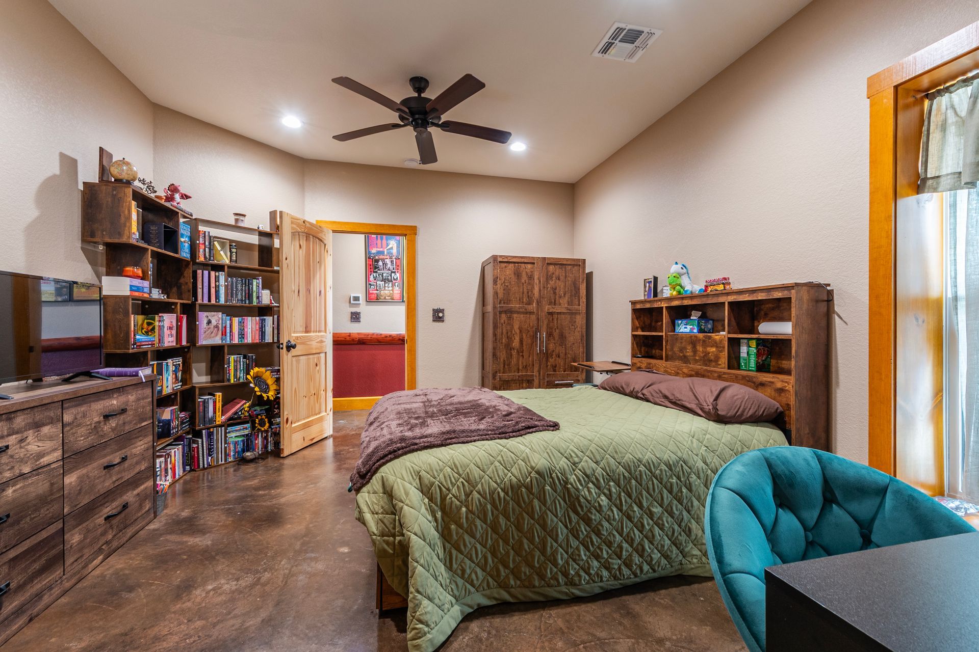 Bedroom with bed, bookshelves, wardrobe, desk, and open doorway; neutral tones.