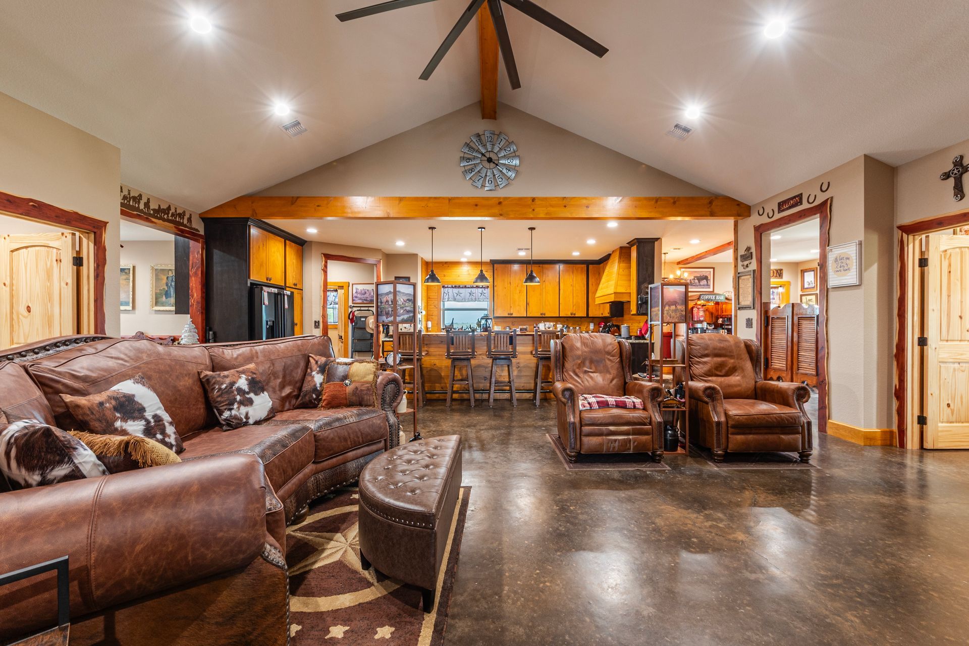 Spacious living room with brown leather furniture, open kitchen, and a rustic, warm decor.