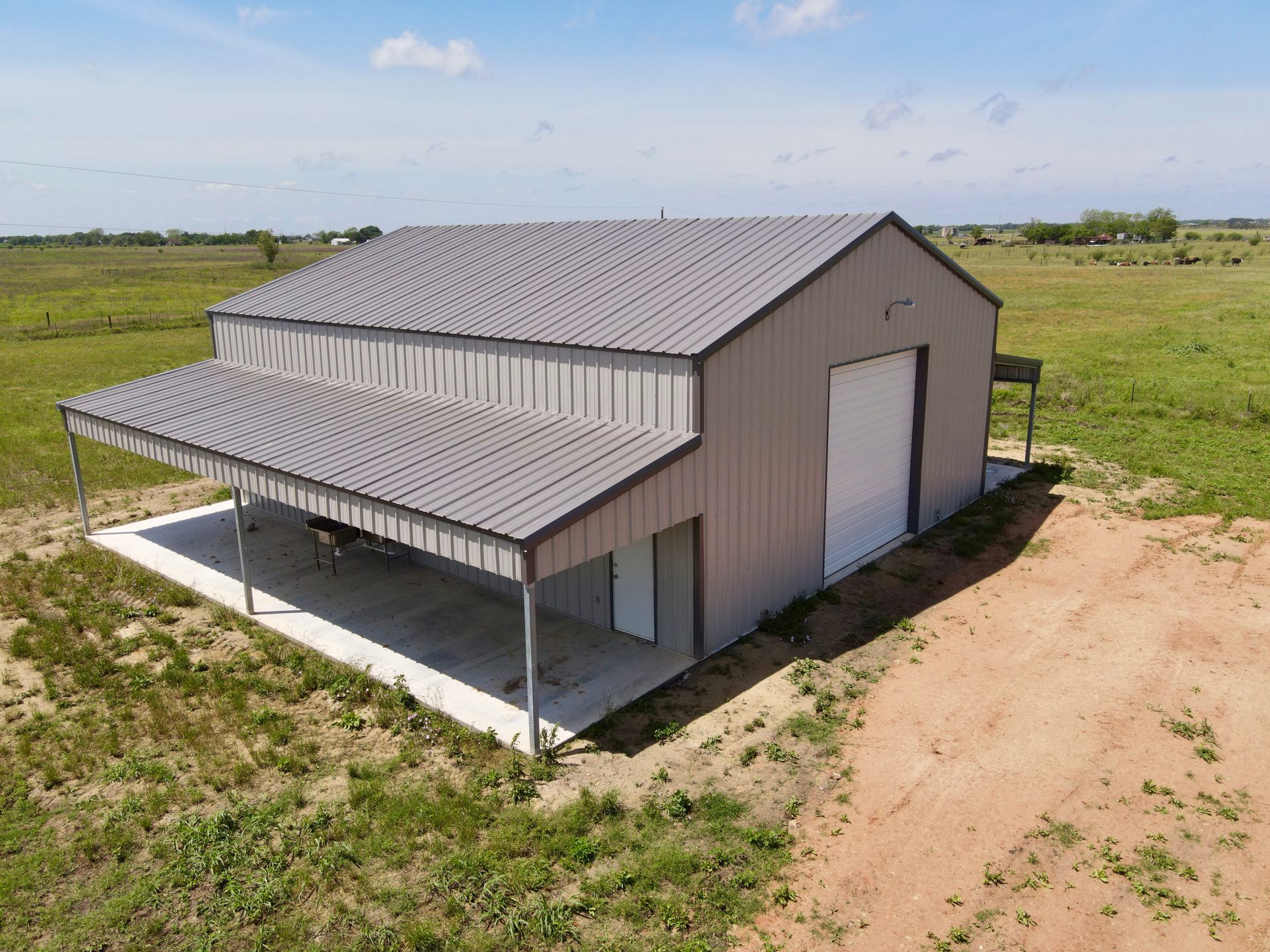 Metal barn with covered porch, in a field under a blue sky.