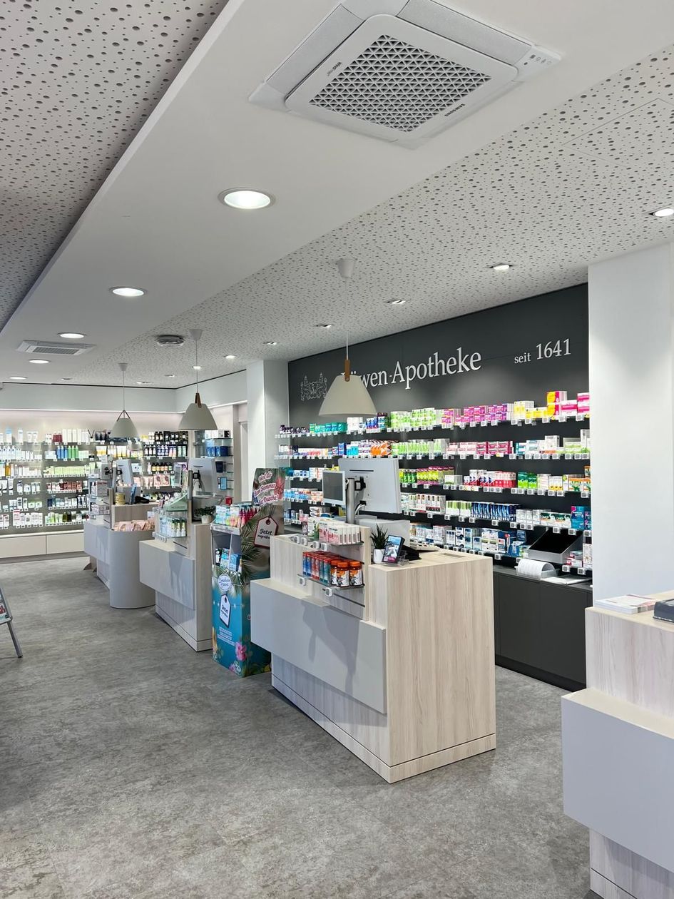 Innenansicht einer modernen Apotheke mit Bedientheken, Regalen mit Waren und einer grauen, strukturierten Decke.