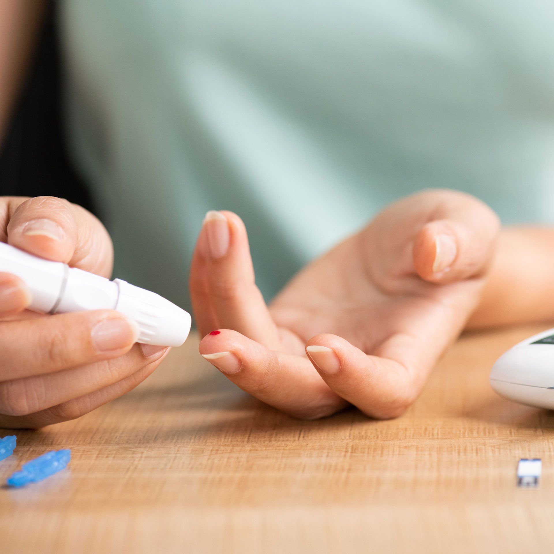 Eine Person benutzt eine weiße Lanzette, um sich in den Finger zu stechen und so einen kleinen Blutstropfen für einen Glukosetest zu gewinnen.