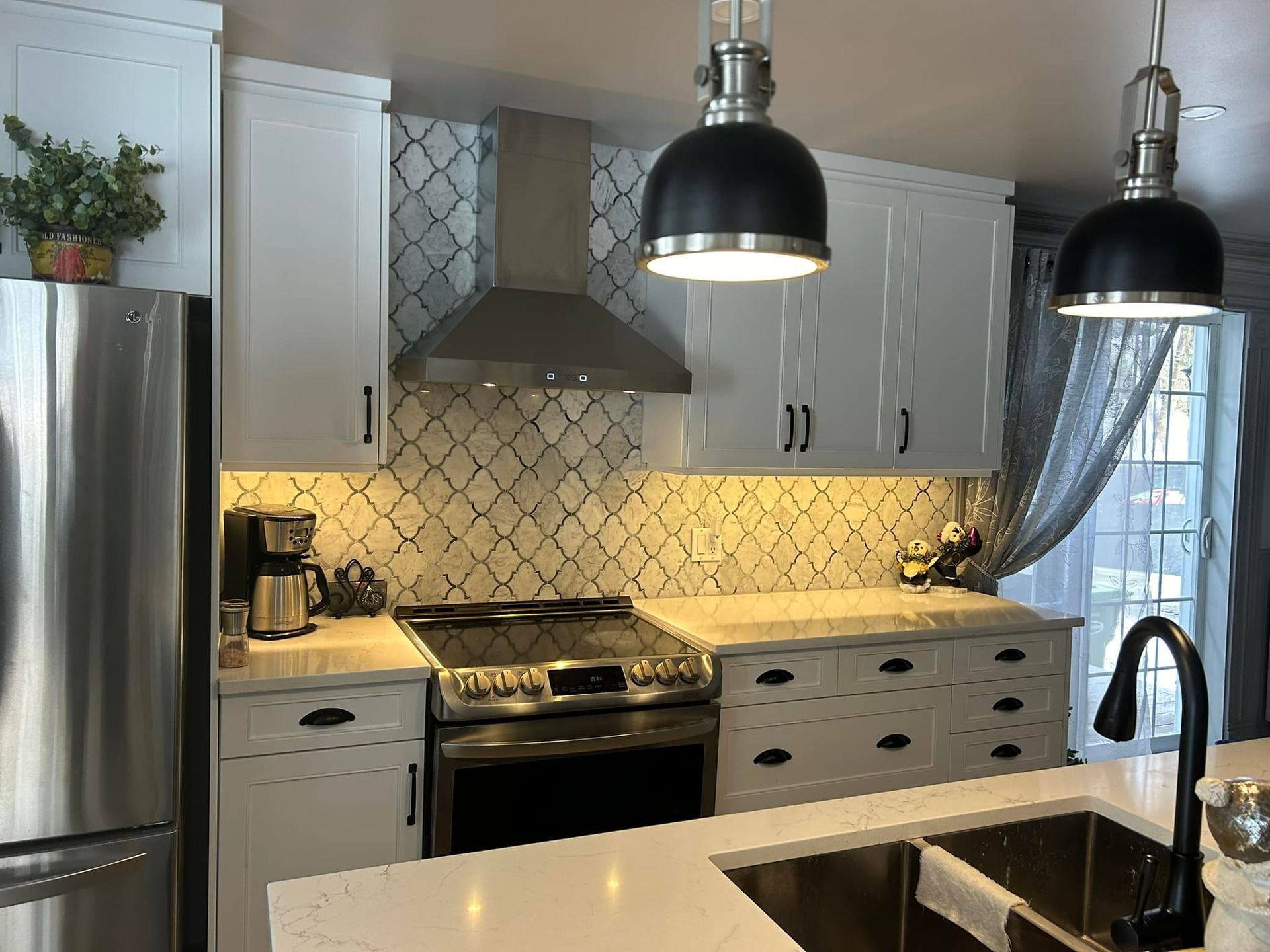 Une cuisine avec des armoires blanches, des appareils électroménagers en acier inoxydable, un évier et une cuisinière.