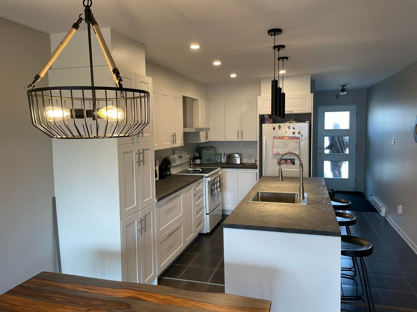 Une cuisine avec des armoires blanches, un évier, un réfrigérateur et un lustre suspendu au plafond.