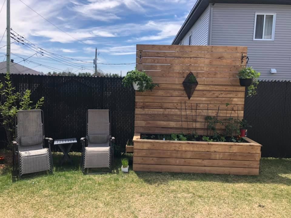 Deux chaises sont assises dans une cour arrière à côté d'un mur en bois.