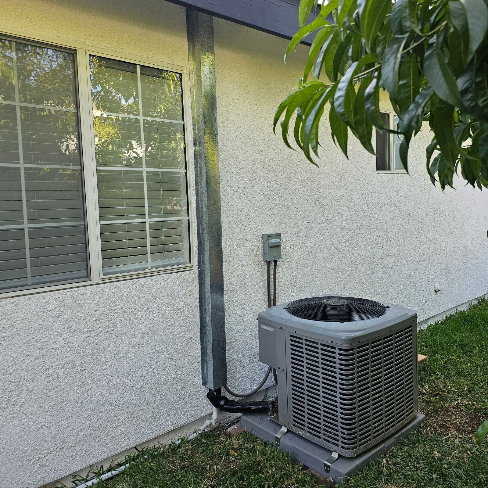 An air conditioner is sitting on the side of a house next to a window.