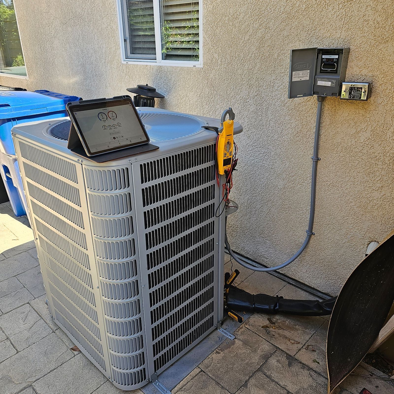 An air conditioner is sitting outside of a house with a tablet on top of it.