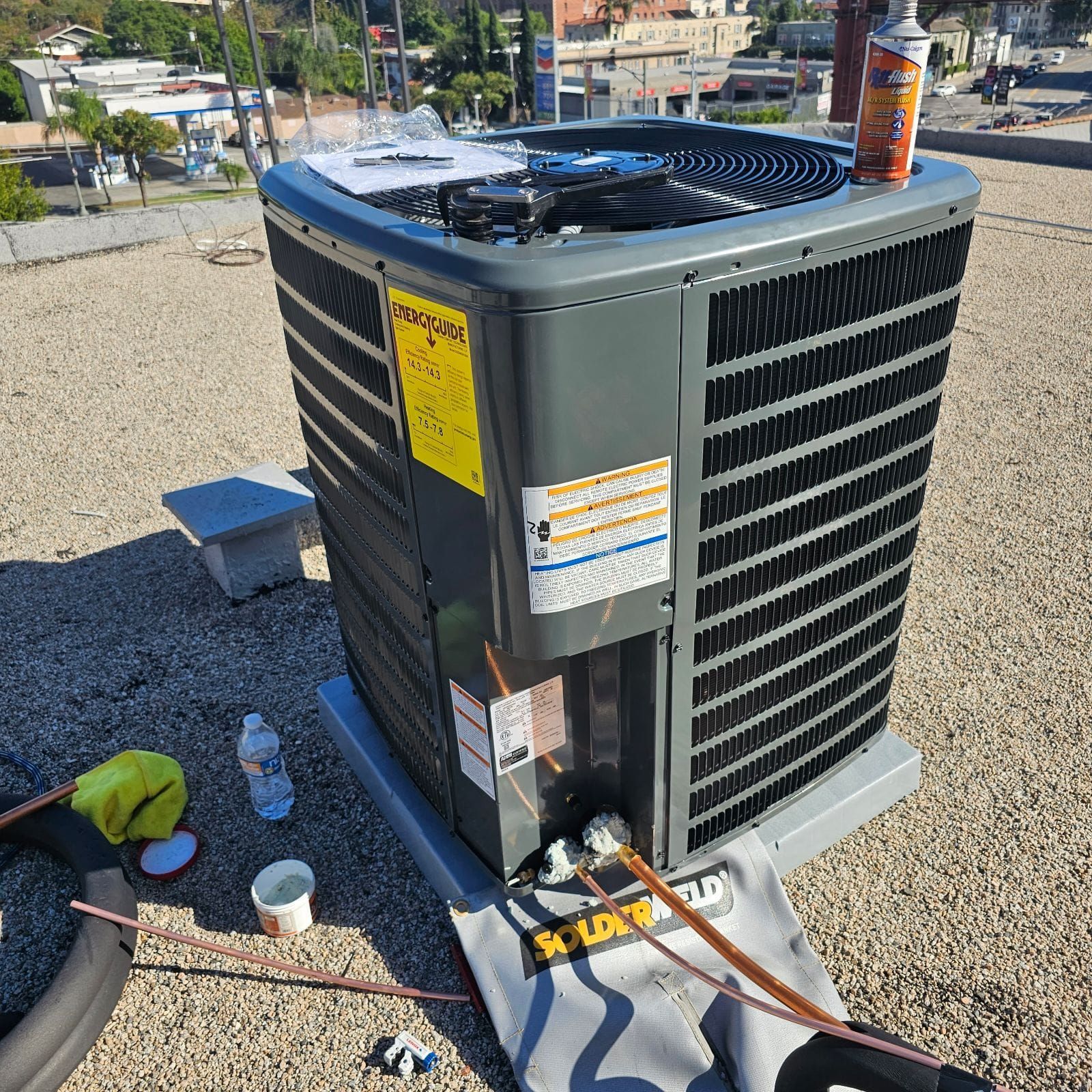 A large air conditioner is sitting on top of a gravel roof.