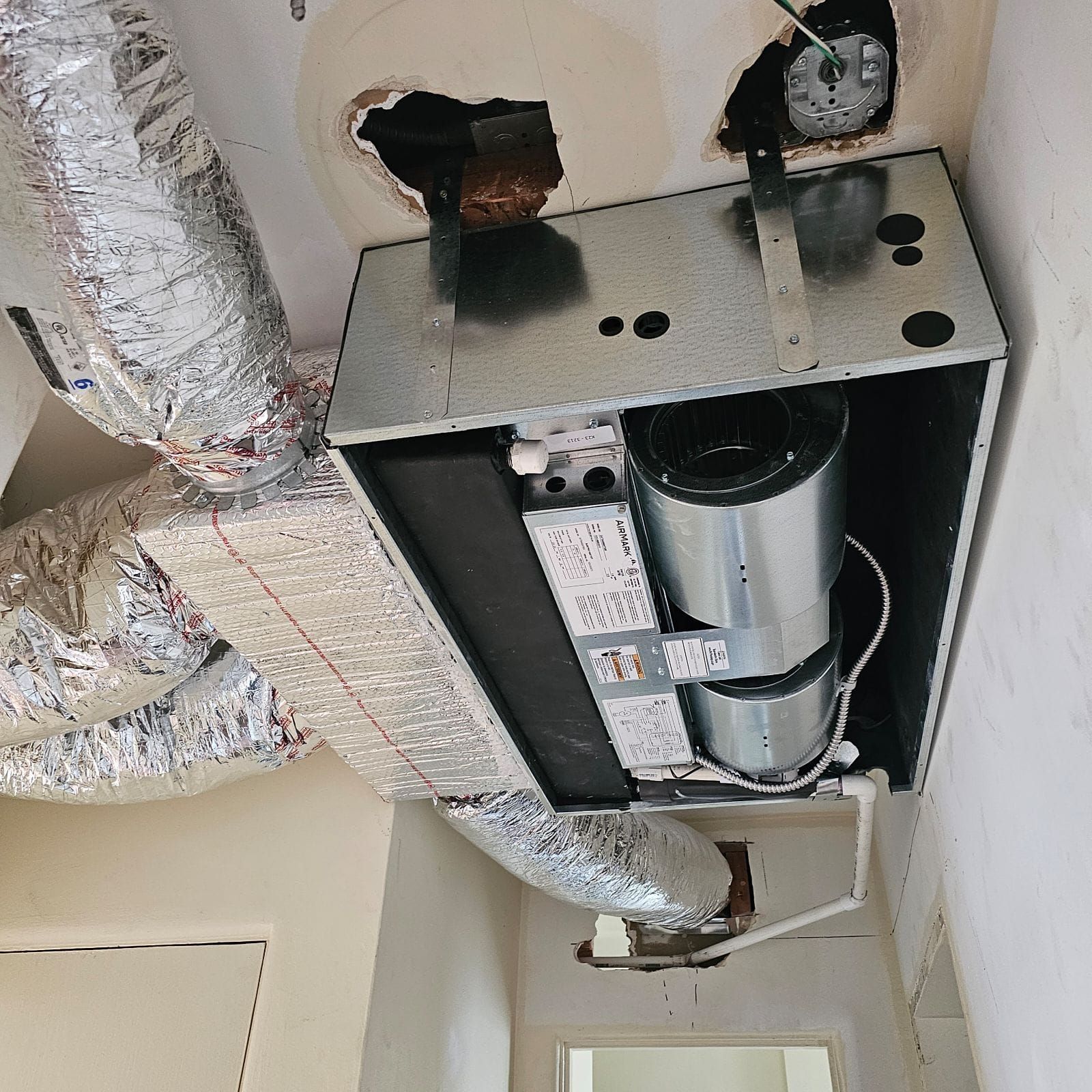 There is a hole in the ceiling of a room with ducts coming out of it.