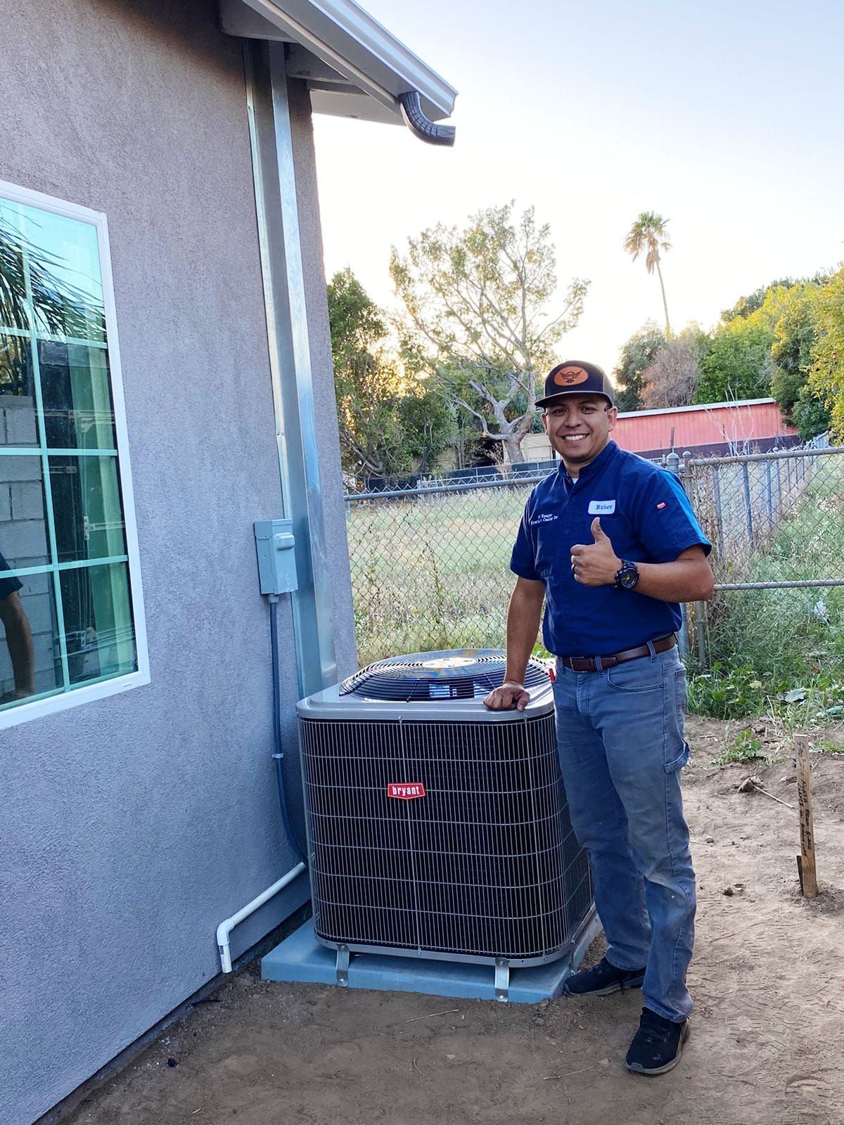 A man is standing next to an air conditioner and giving a thumbs up.