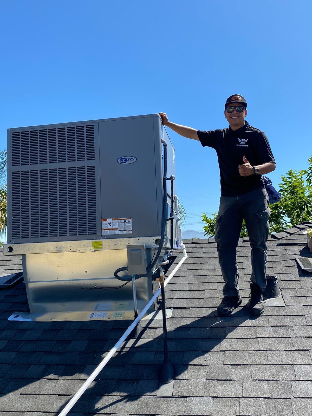 A man is standing on top of a roof next to a large air conditioner.