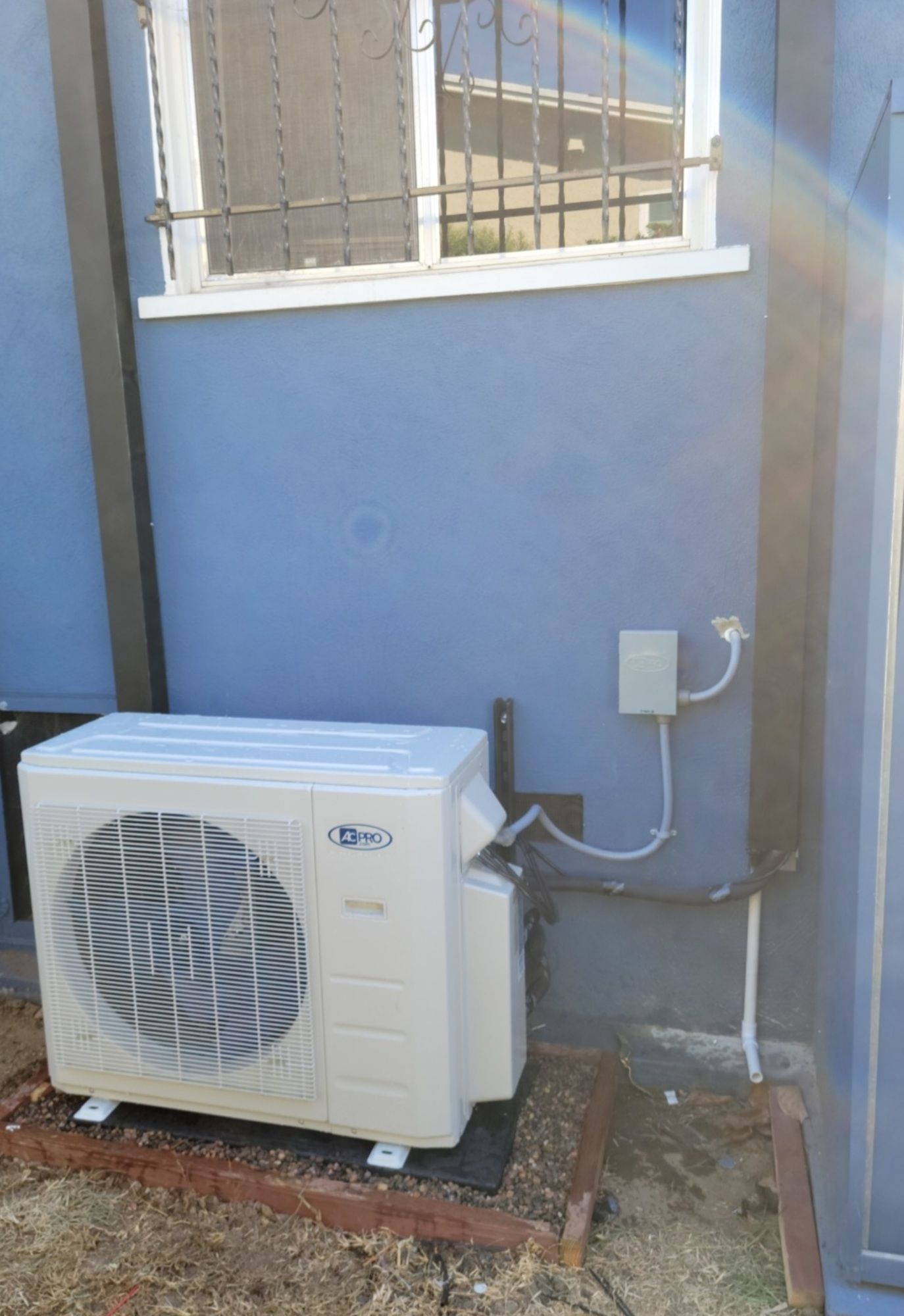A white air conditioner is sitting outside of a blue building next to a window.