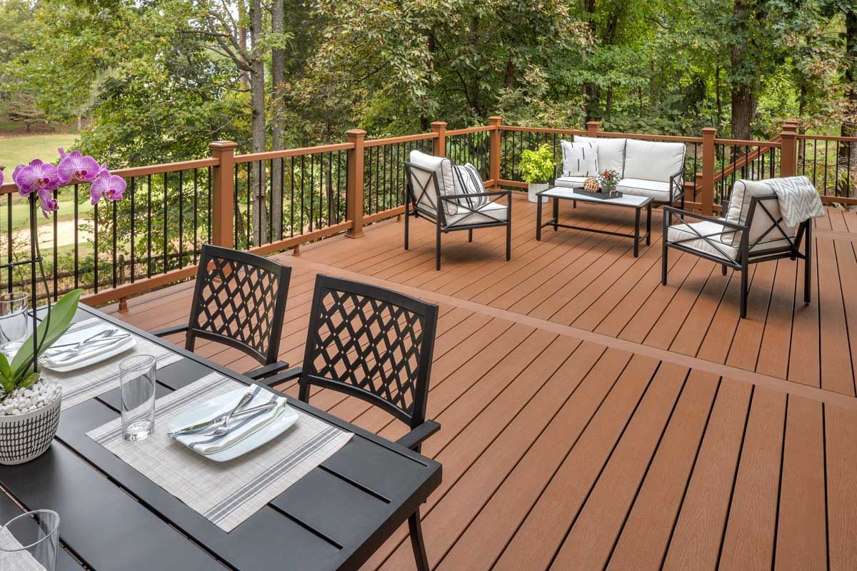 Trex® Decking from Budget Home Supply Colorado - Outdoor deck with seating, dining table, and trees in background. Brown deck, metal furniture.