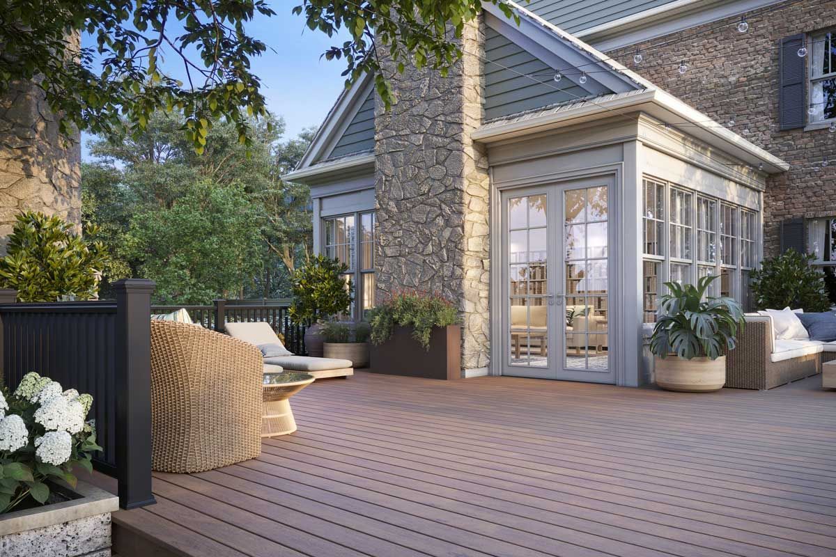 Trex® Decking from Budget Home Supply Colorado - Composite deck with outdoor furniture, stone chimney, and glass doors leading into a house.