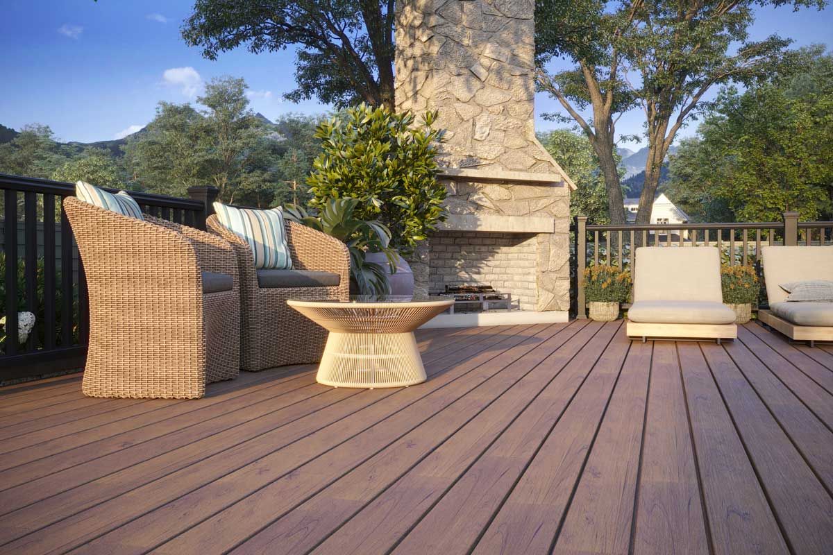 Trex® Decking from Budget Home Supply Colorado - Outdoor deck with wicker furniture, stone fireplace, and wooded background.