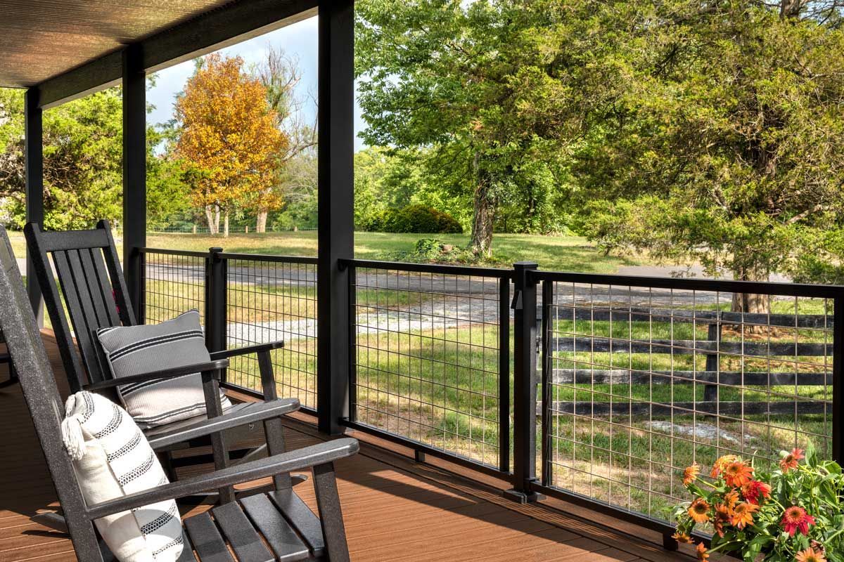 Trex® Decking from Budget Home Supply Colorado - Porch with rocking chairs, overlooking a field with trees, black railing, flowers in a pot, blue sky.