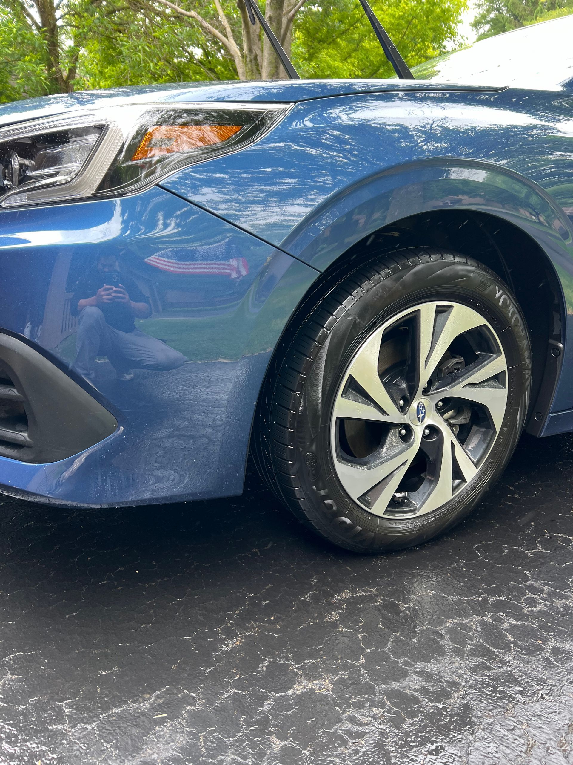 A blue car is parked in a driveway with trees in the background.