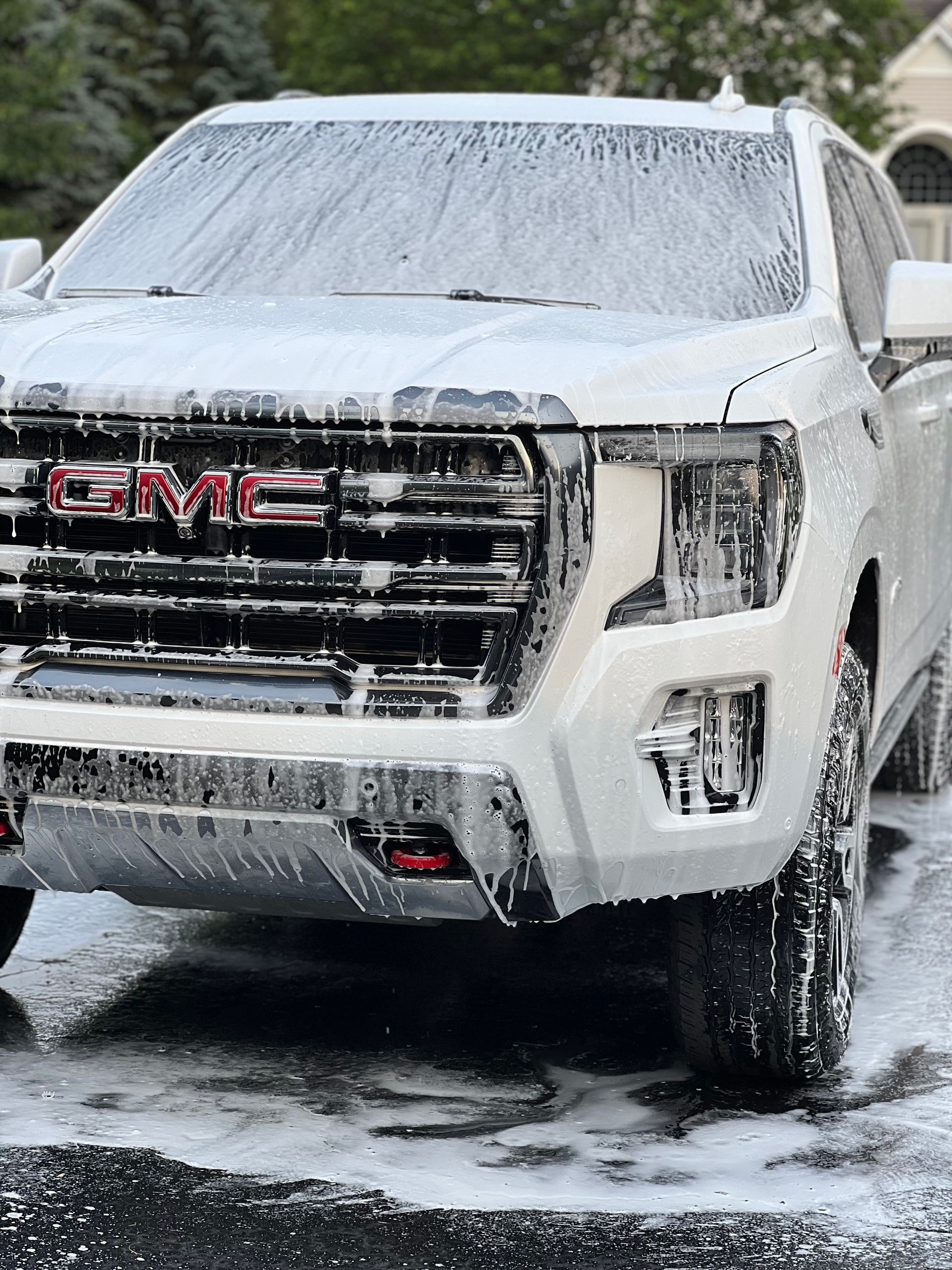 A white gmc truck is covered in foam in a parking lot.