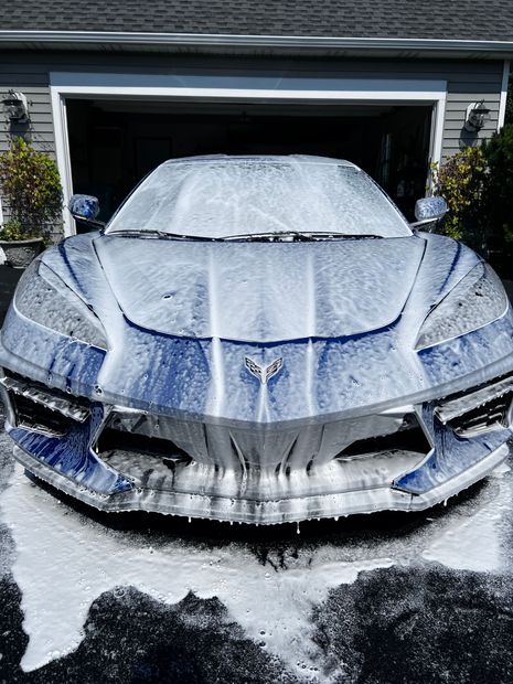 A blue sports car is covered in foam in front of a garage.