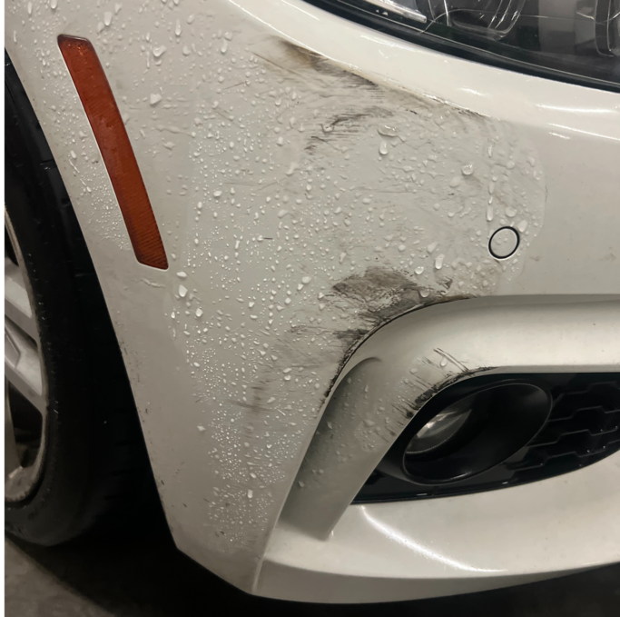 A white car with a damaged bumper is parked in a garage.