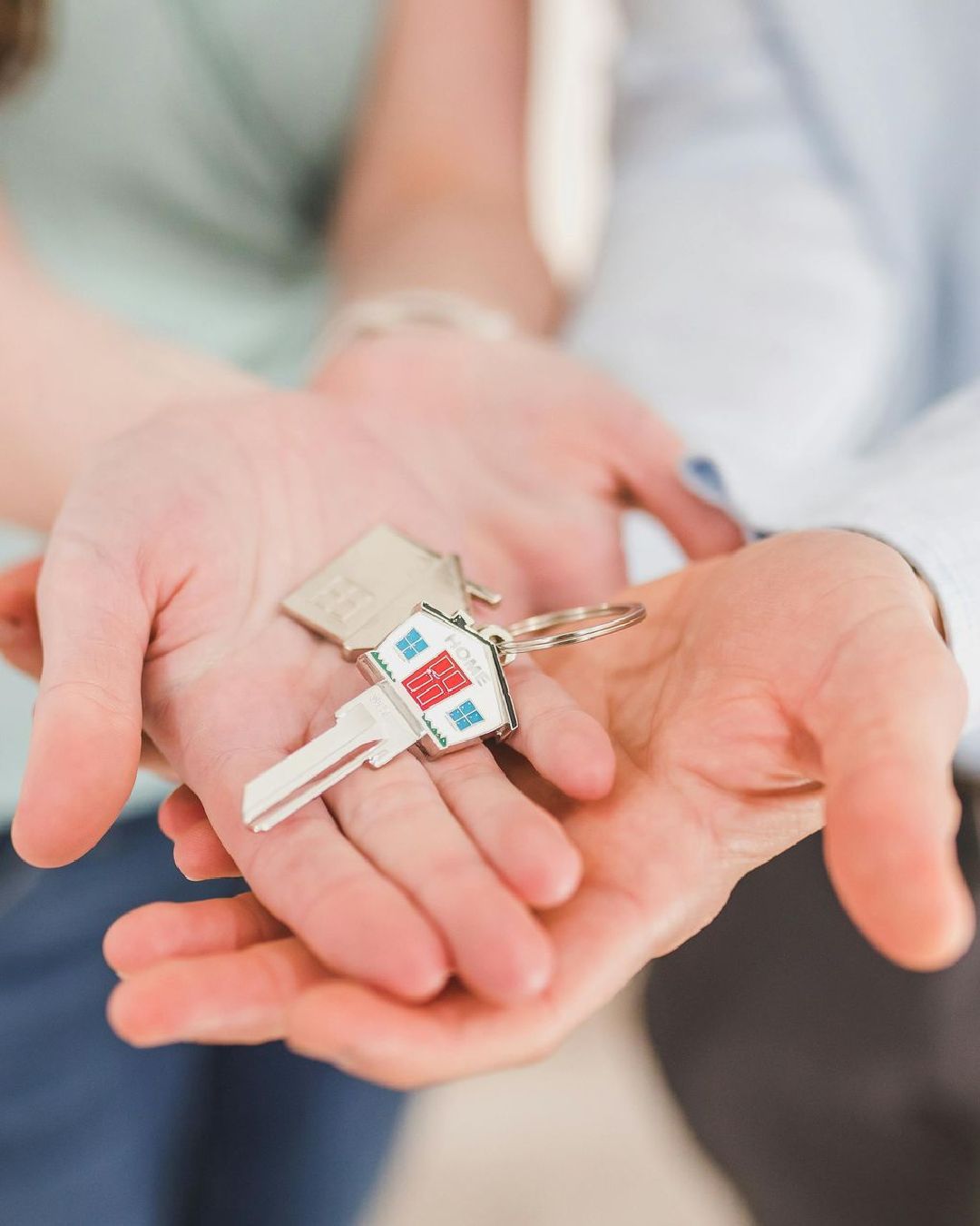 Hands holding house keys with a home-shaped keychain.