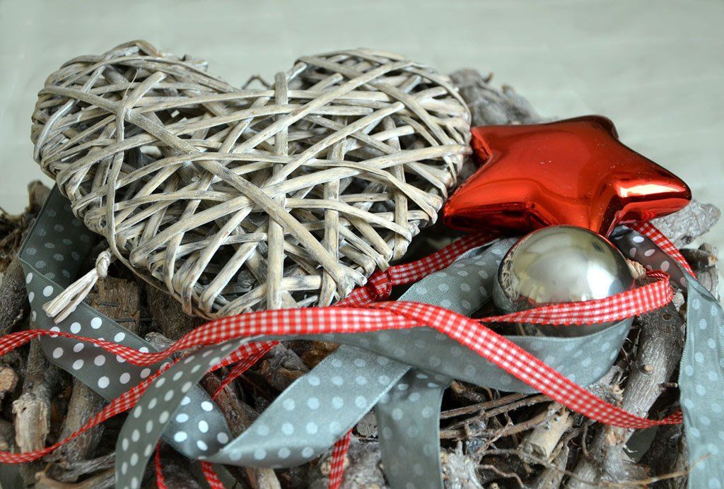 Wicker heart with Christmas ribbons, red star, and silver ornament on rustic wood.