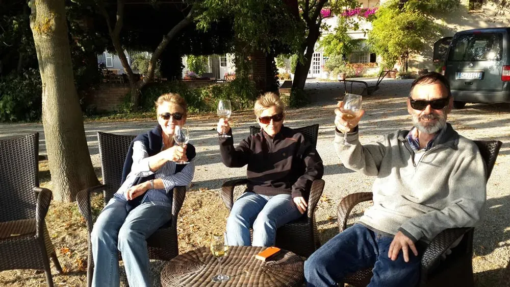 Three people relax on wicker chairs by a rustic building and van.