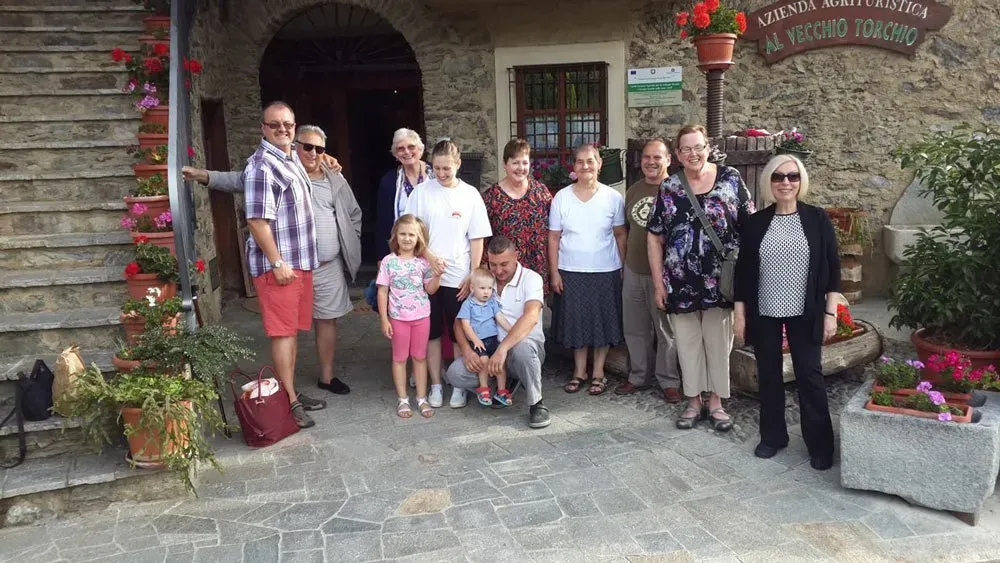 Group photo in front of a rustic agriturismo with stone walls and flower pots, labeled “Al Vecchio Torchio.”